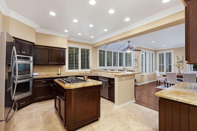 kitchen with appliances with stainless steel finishes, a sink, tasteful backsplash, a kitchen island, and ornamental molding