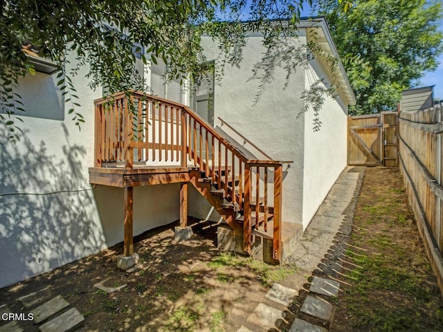 rear view of house with fence, a gate, stucco siding, and stairway