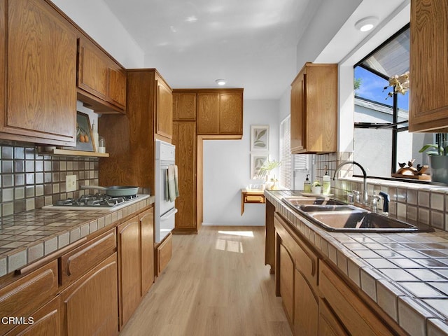 kitchen featuring backsplash, tile countertops, light wood-type flooring, a sink, and white appliances