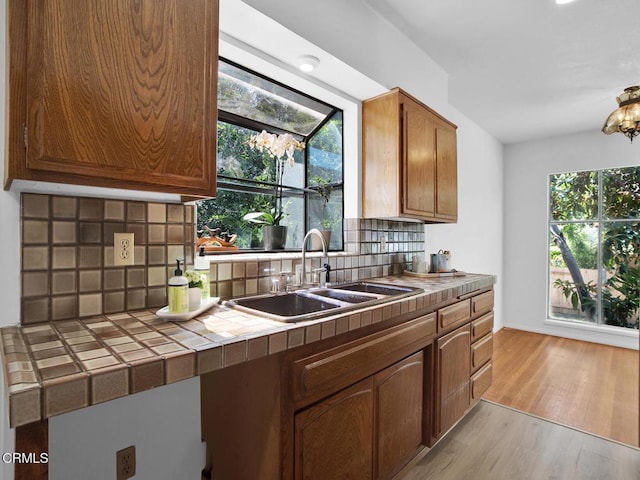 kitchen featuring backsplash, tile countertops, brown cabinets, a sink, and light wood-style flooring