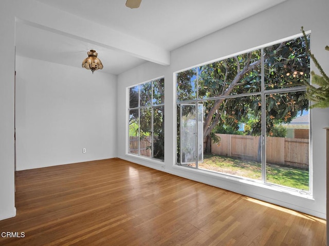spare room featuring beamed ceiling, an inviting chandelier, and wood finished floors