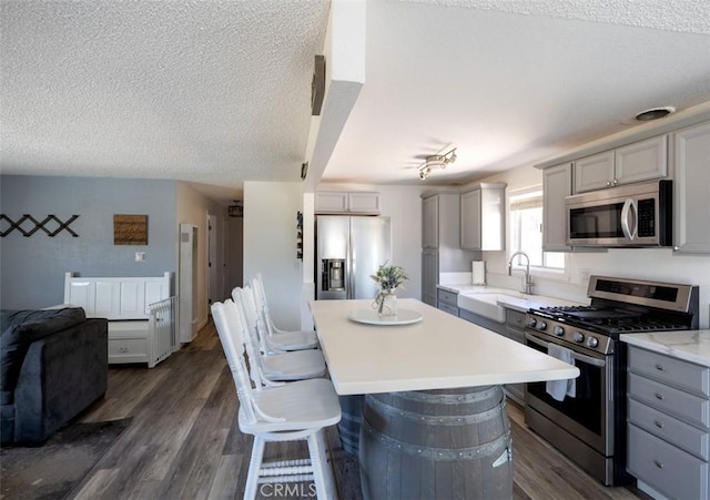 kitchen featuring a sink, stainless steel appliances, dark wood-type flooring, light countertops, and gray cabinetry