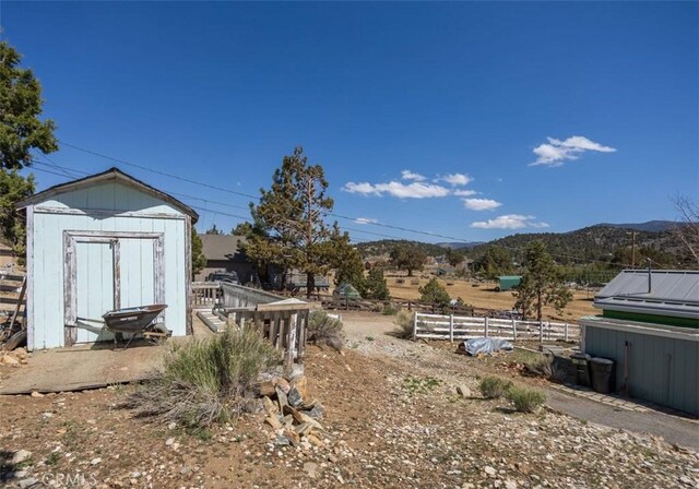 view of yard featuring an outdoor structure, a storage shed, a mountain view, and fence