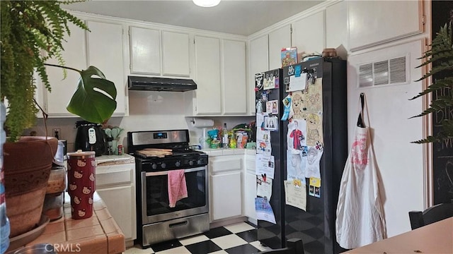 kitchen with stainless steel gas range, tile counters, freestanding refrigerator, and under cabinet range hood