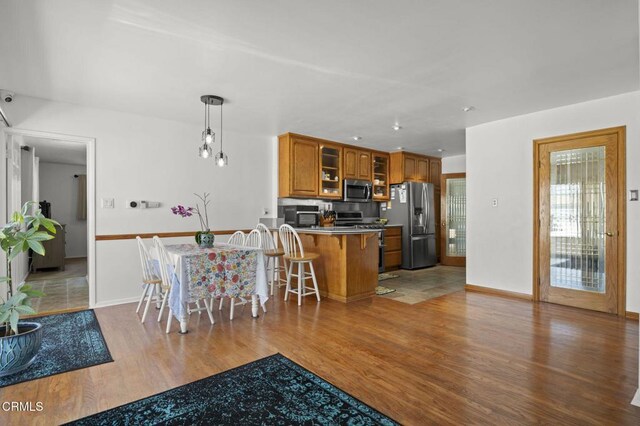 1213 Doris Ave, Oxnard, CA 93030 - kitchen with stainless steel appliances, brown cabinetry, wood finished floors, glass insert cabinets, and a peninsula