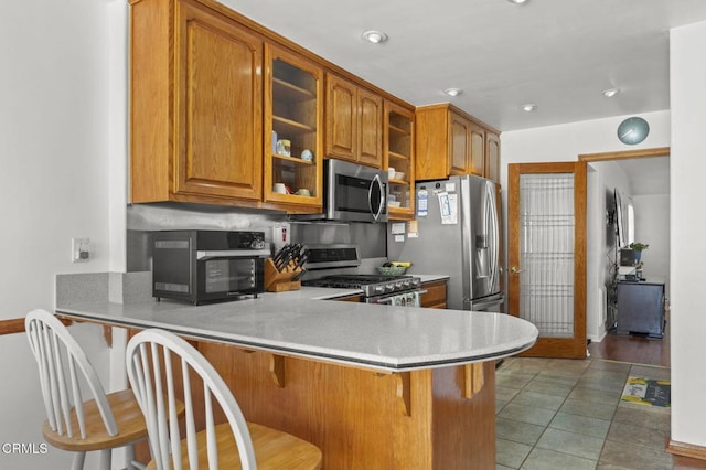 1213 Doris Ave, Oxnard, CA 93030 - kitchen with stainless steel appliances, brown cabinets, glass insert cabinets, a peninsula, and a kitchen bar