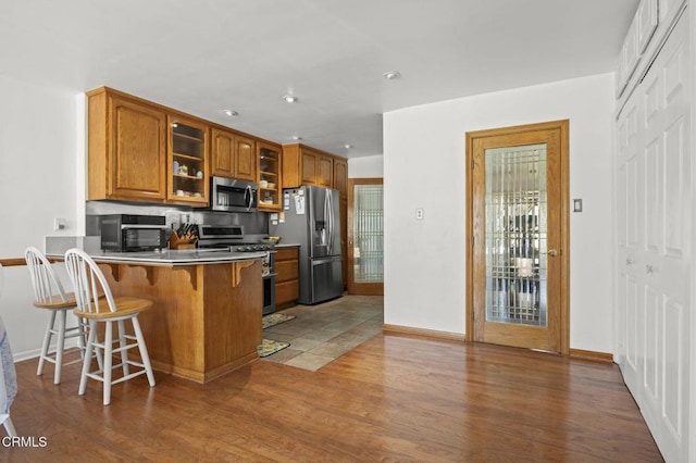1213 Doris Ave, Oxnard, CA 93030 - kitchen featuring appliances with stainless steel finishes, brown cabinetry, glass insert cabinets, a kitchen breakfast bar, and wood finished floors