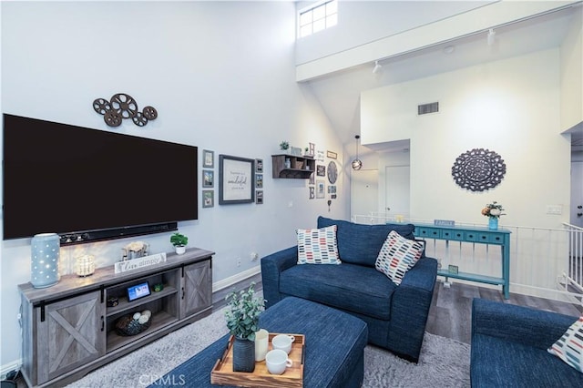 living area featuring track lighting, baseboards, wood finished floors, a towering ceiling, and visible vents