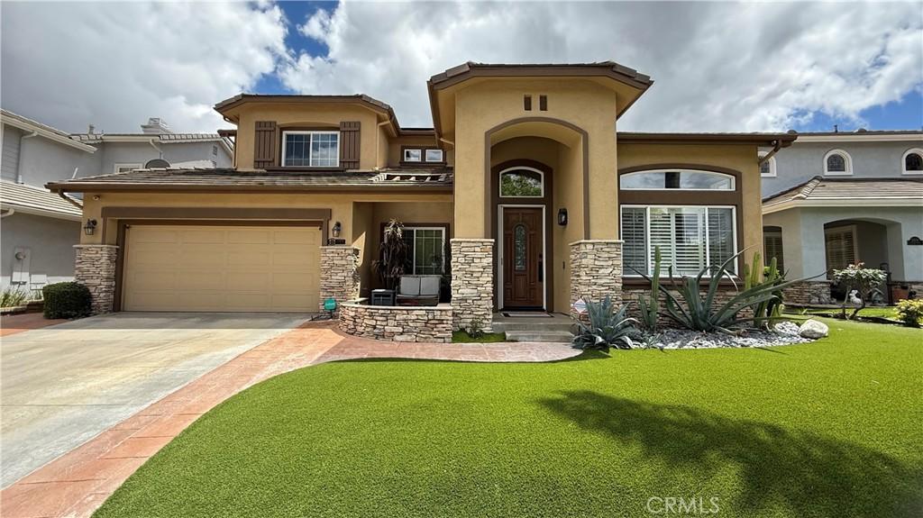 mediterranean / spanish-style home with a front yard, driveway, stone siding, and stucco siding