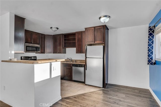 kitchen featuring dark brown cabinets, baseboards, light wood-type flooring, a sink, and appliances with stainless steel finishes