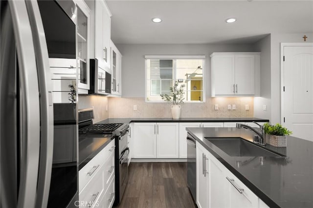 kitchen with stainless steel appliances, dark countertops, a sink, recessed lighting, and dark wood-style floors