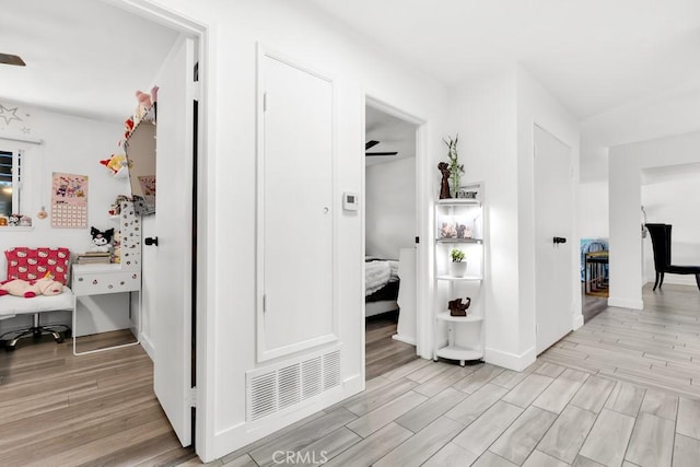 hallway featuring light wood finished floors, baseboards, and visible vents