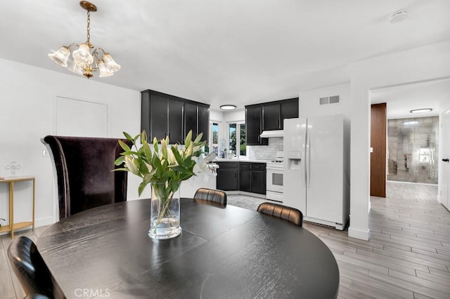dining room featuring baseboards, a chandelier, visible vents, and light wood-style flooring