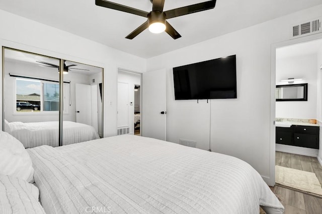 bedroom featuring ceiling fan, ensuite bathroom, visible vents, and wood finished floors