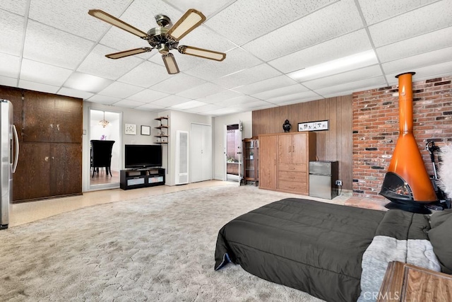 bedroom with freestanding refrigerator, wood walls, a wood stove, and a drop ceiling