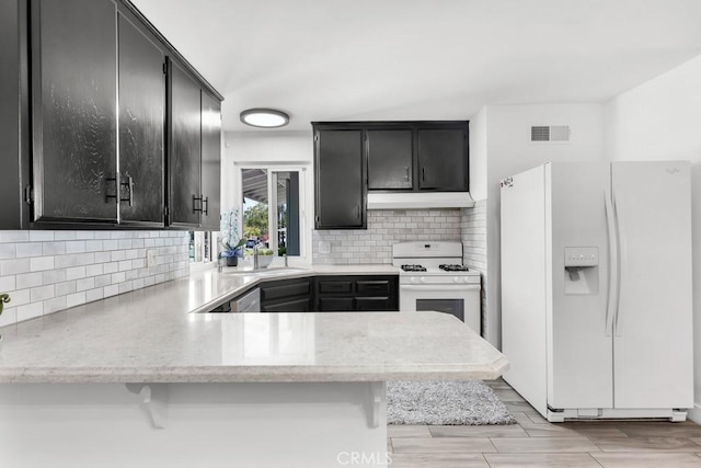 kitchen with white appliances, dark cabinets, visible vents, and under cabinet range hood