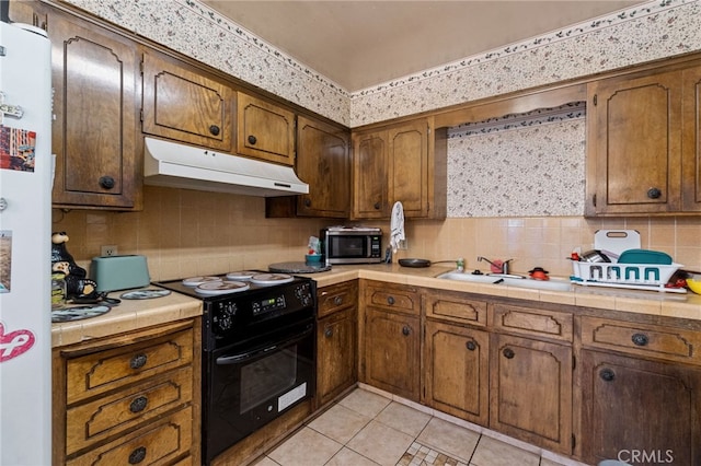kitchen with stainless steel microwave, tasteful backsplash, under cabinet range hood, tile countertops, and black / electric stove