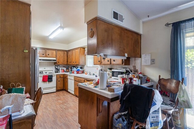 kitchen with brown cabinets, visible vents, under cabinet range hood, white appliances, and a peninsula