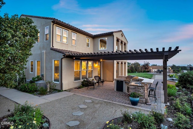 20752 Veneto Way, Porter Ranch, CA 91326 - back of property at dusk with area for grilling, a pergola, a patio area, stucco siding, and a tiled roof