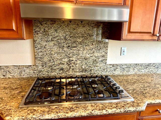 details with decorative backsplash, stainless steel gas cooktop, under cabinet range hood, and light stone countertops