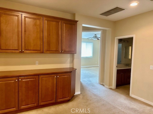 kitchen featuring light carpet, brown cabinetry, a ceiling fan, baseboards, and visible vents