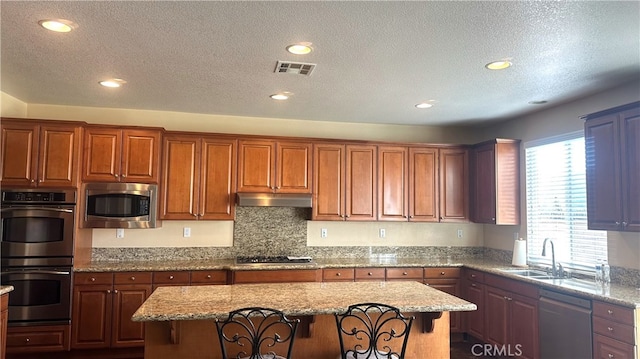 kitchen featuring visible vents, a center island, a textured ceiling, under cabinet range hood, and appliances with stainless steel finishes