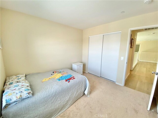 bedroom with baseboards, visible vents, light colored carpet, and a closet