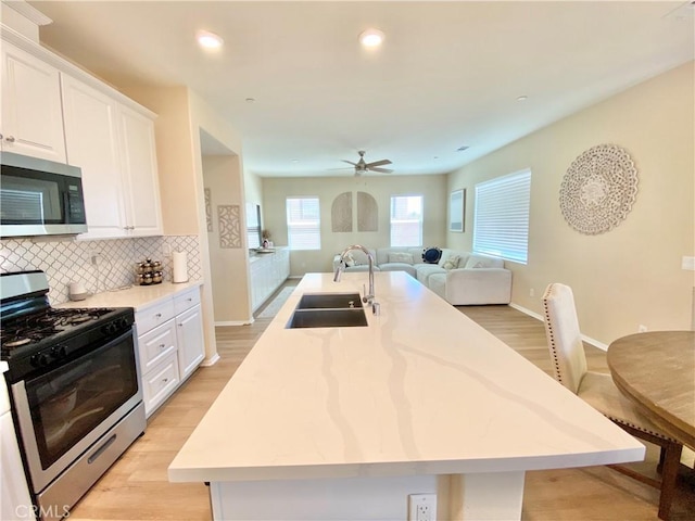 kitchen with a kitchen island with sink, a sink, white cabinets, and stainless steel appliances