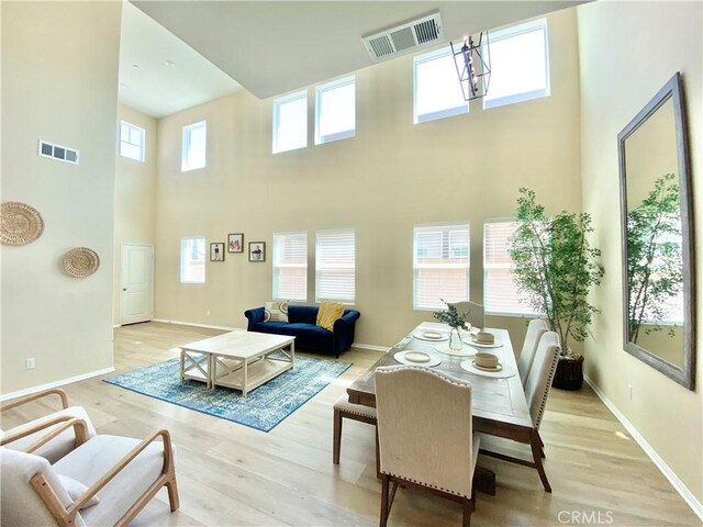 living area with a high ceiling, visible vents, light wood-style flooring, and baseboards