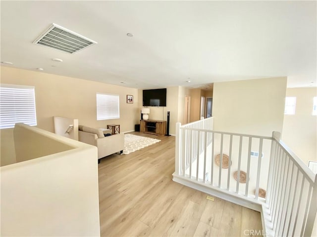 hallway with visible vents, an upstairs landing, and light wood-style flooring