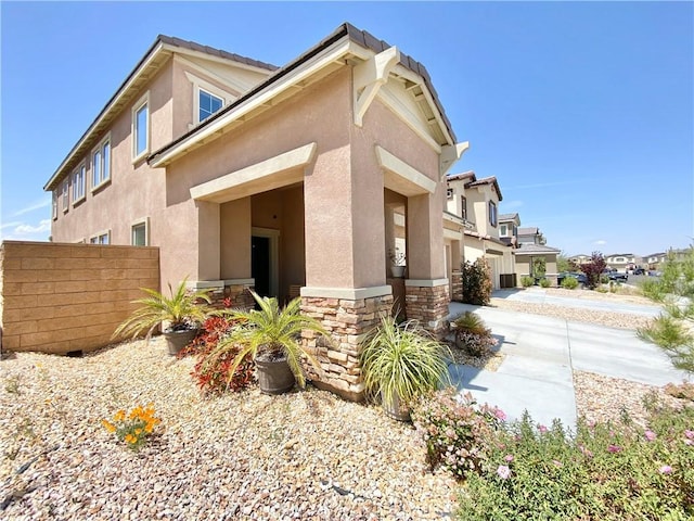 view of property exterior with stucco siding, fence, concrete driveway, and stone siding