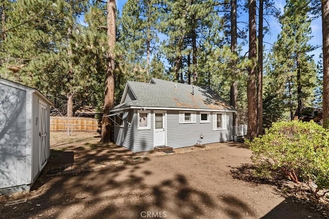 rear view of property with fence, an outdoor structure, entry steps, and a shingled roof
