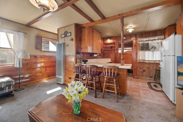 kitchen featuring a heating unit, wood walls, freestanding refrigerator, beam ceiling, and a peninsula