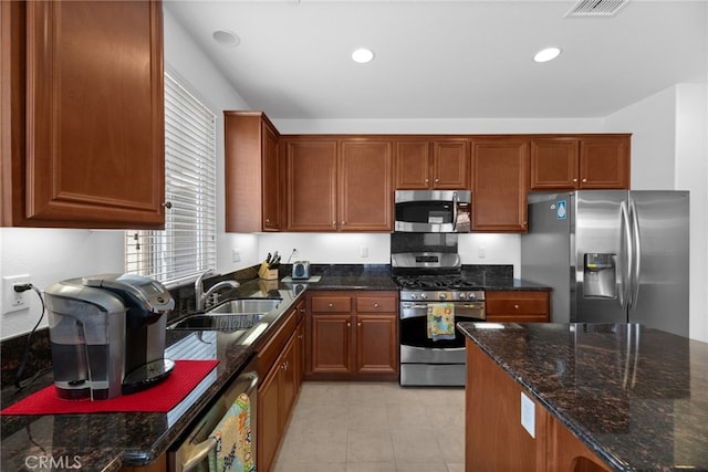 kitchen featuring dark stone countertops, light tile patterned floors, a sink, visible vents, and stainless steel appliances
