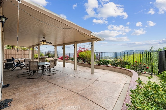 view of patio / terrace featuring outdoor dining space, a ceiling fan, a mountain view, and a fenced backyard