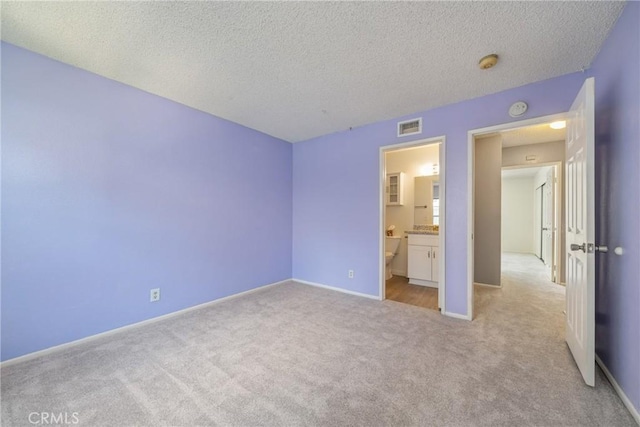 unfurnished bedroom with connected bathroom, visible vents, light carpet, baseboards, and a textured ceiling