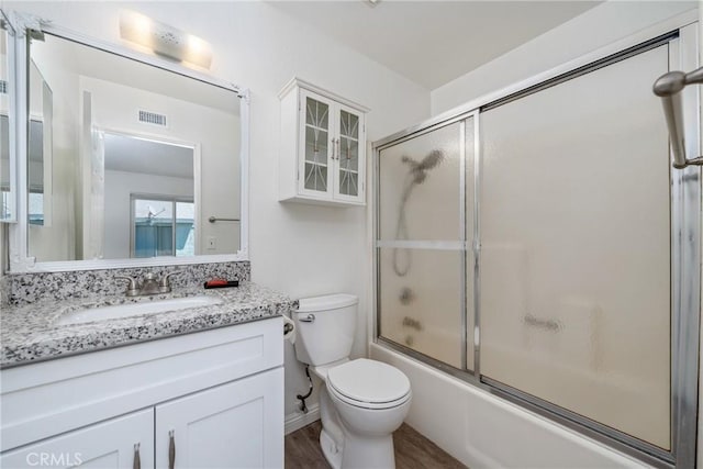 full bathroom with vanity, toilet, visible vents, enclosed tub / shower combo, and wood finished floors