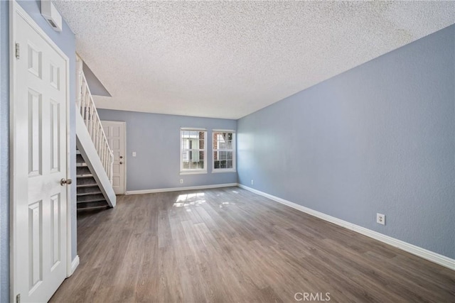 unfurnished living room with baseboards, stairway, wood finished floors, and a textured ceiling