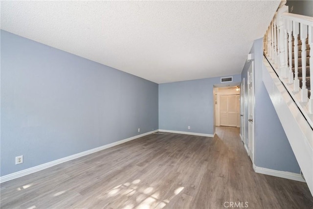 unfurnished room featuring a textured ceiling, visible vents, baseboards, wood finished floors, and stairs