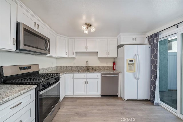 kitchen featuring a sink, light wood-style floors, light stone counters, white cabinetry, and appliances with stainless steel finishes