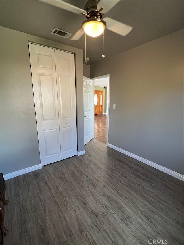 unfurnished bedroom with dark wood-type flooring, visible vents, a closet, and baseboards