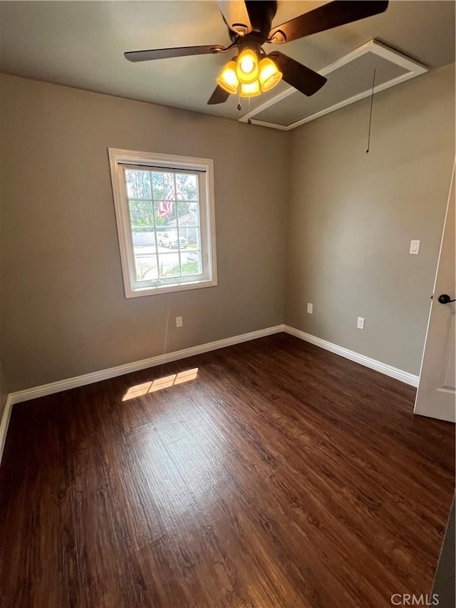 spare room featuring attic access, dark wood-type flooring, ceiling fan, and baseboards