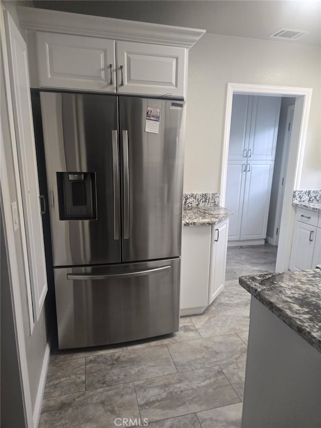 kitchen featuring white cabinetry, visible vents, stainless steel fridge, and stone counters