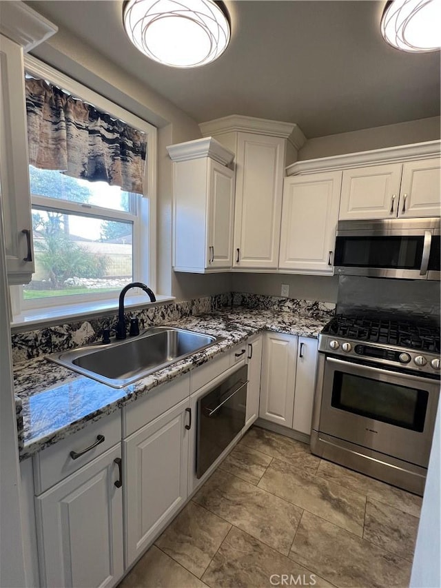 kitchen featuring stone countertops, a sink, appliances with stainless steel finishes, and white cabinetry
