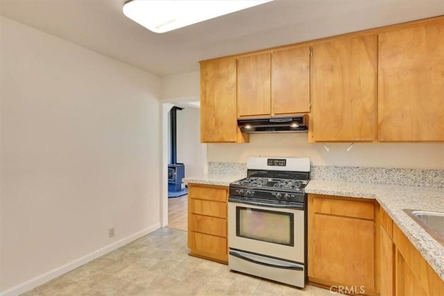 kitchen featuring light stone countertops, gas range, under cabinet range hood, baseboards, and a wood stove