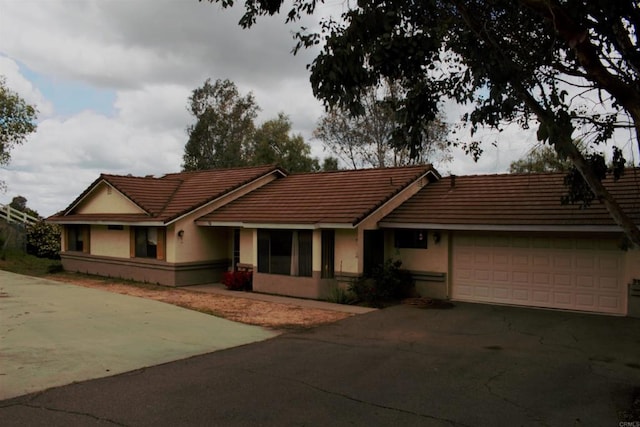 view of front facade featuring stucco siding, a tiled roof, and aphalt driveway