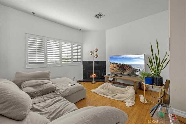 living area featuring visible vents, wood finished floors, and a lit fireplace