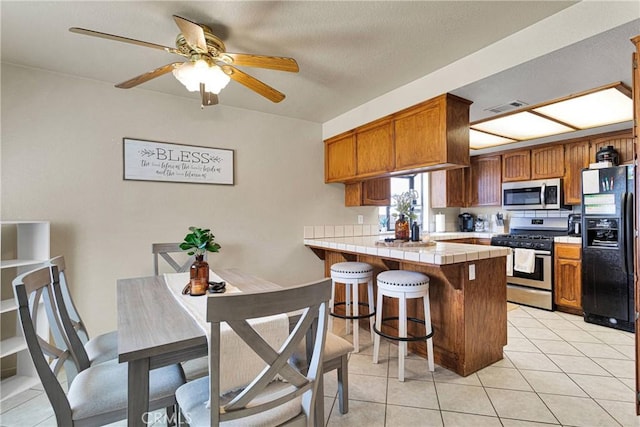 kitchen with stainless steel appliances, tile counters, brown cabinets, visible vents, and a peninsula