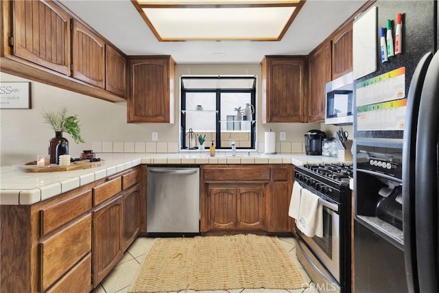 kitchen featuring light tile patterned floors, brown cabinets, a sink, and appliances with stainless steel finishes