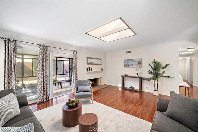 living room with baseboards, a warm lit fireplace, visible vents, and wood finished floors